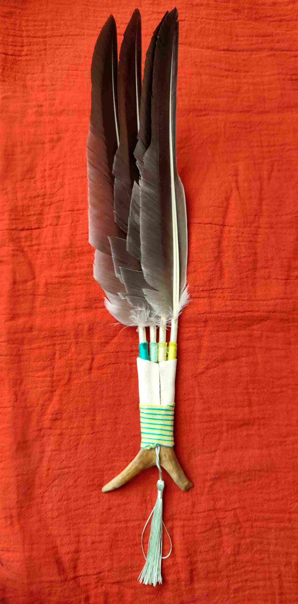Rückseite eines Räucherfächer aus grauen Gänsefedern und Rentierhorn, der auf einem roten Tuch liegt.