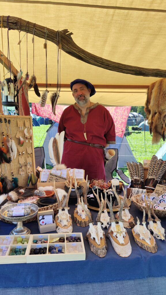 Mittelalterlich gekleideter Mann steht hinter einem dekorierten Marktstand